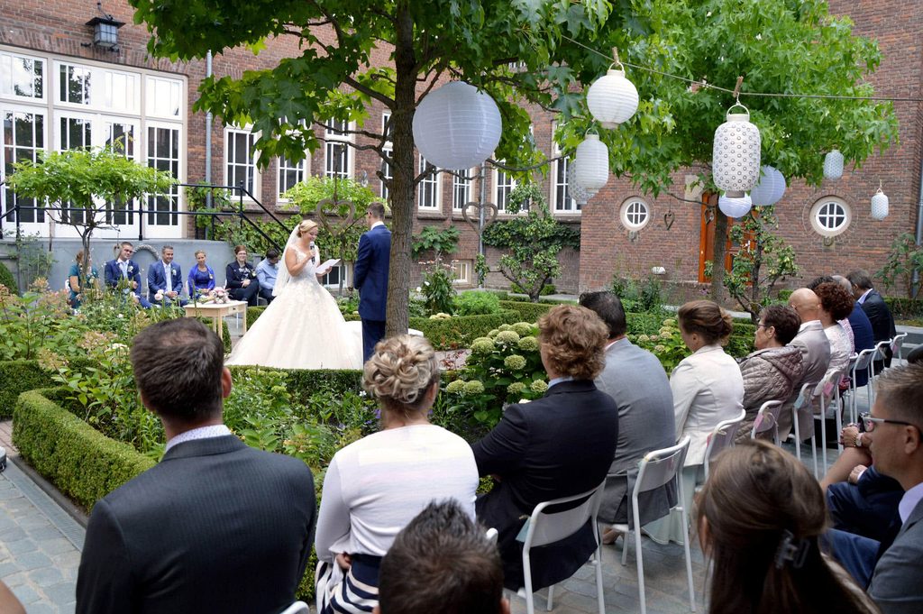 Een ceremonie in de binnentuin: het bruidspaar staat tussen de buxushagen, de gasten zitten op witte stoelen